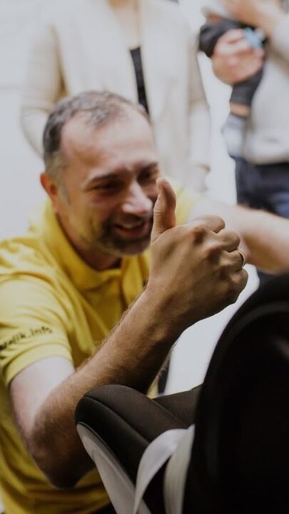 Pawel Kurpiewski pokazuje OK podczas inspekcji bezpieczeństwa fotelika samochodowego, ubrany jest w żółtą koszulkę fotelik.info